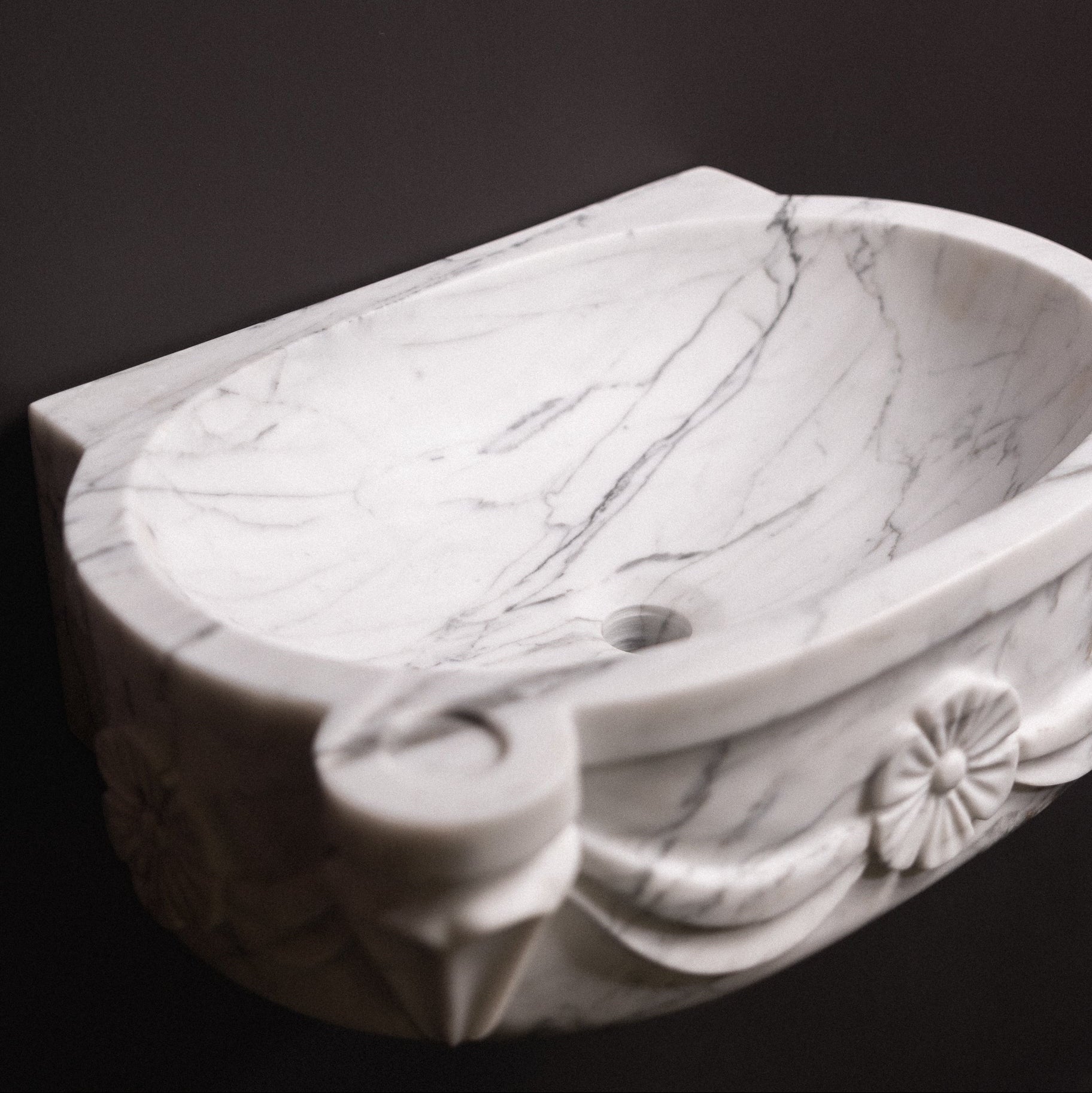 White statuary marble floating wall-mounted sink with floral rosette carvings and draped detailing — luxury hand-carved marble basin for bathrooms.