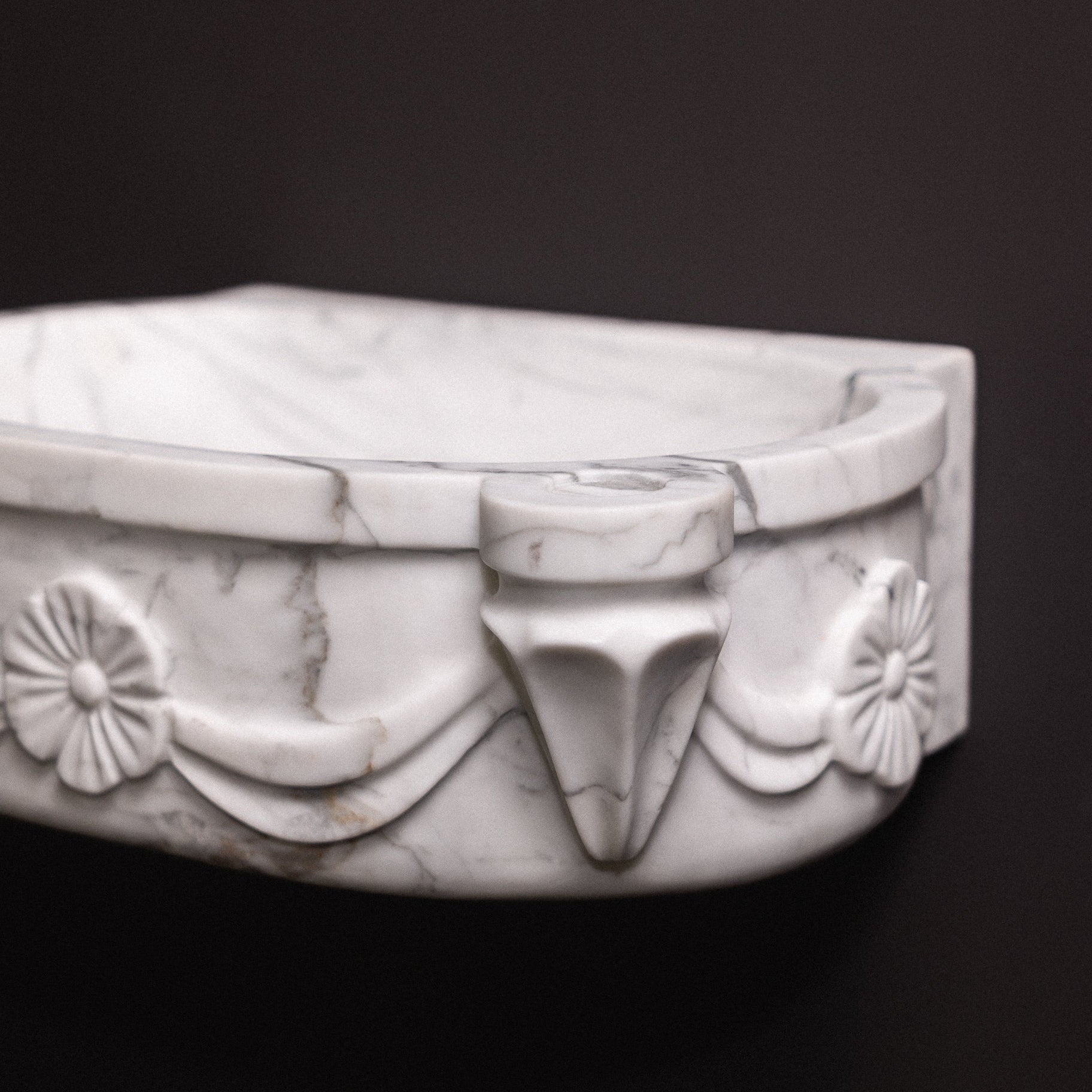 White statuary marble floating wall-mounted sink with floral rosette carvings and draped detailing — luxury hand-carved marble basin for bathrooms.