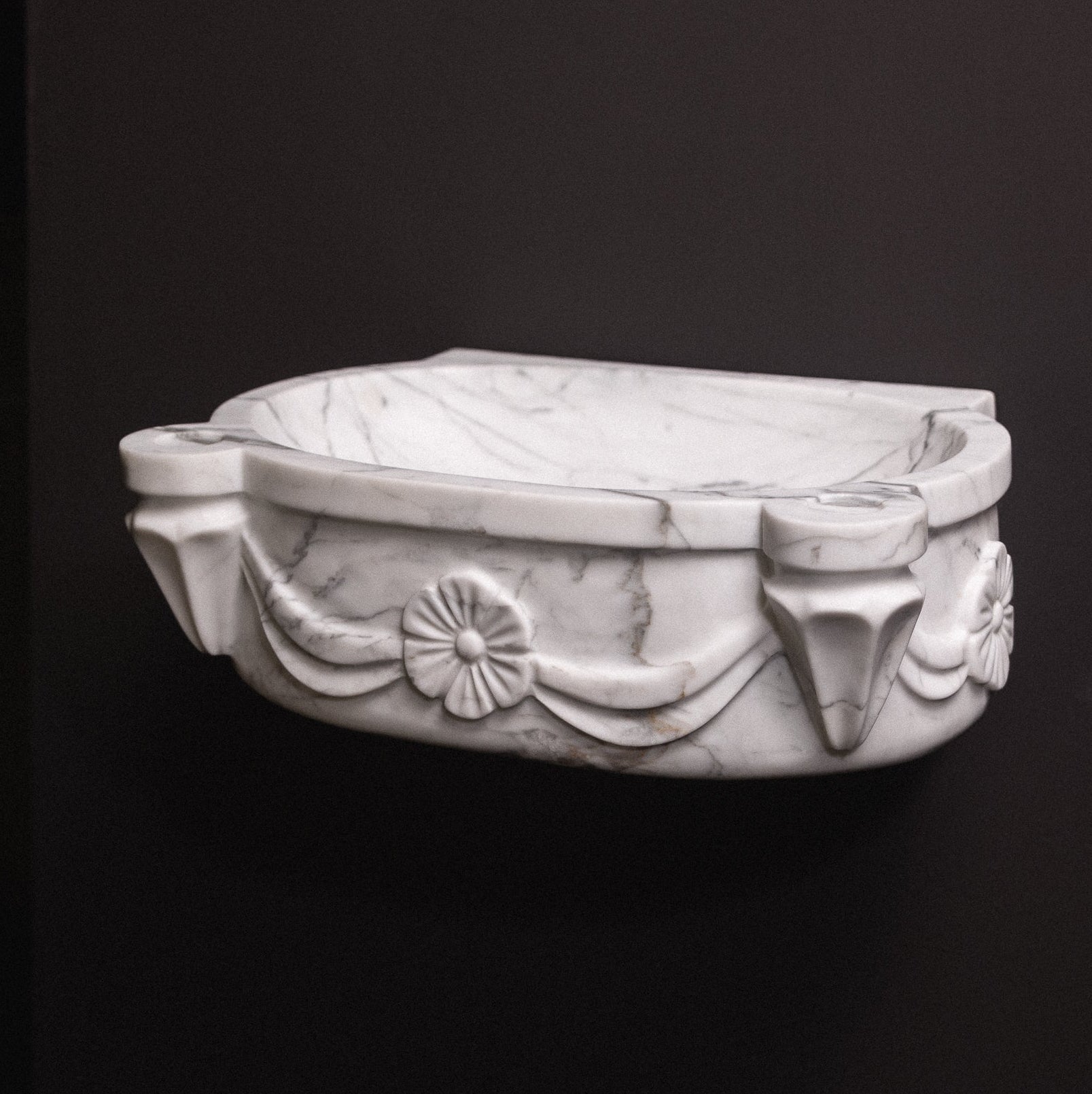 White statuary marble floating wall-mounted sink with floral rosette carvings and draped detailing — luxury hand-carved marble basin for bathrooms.