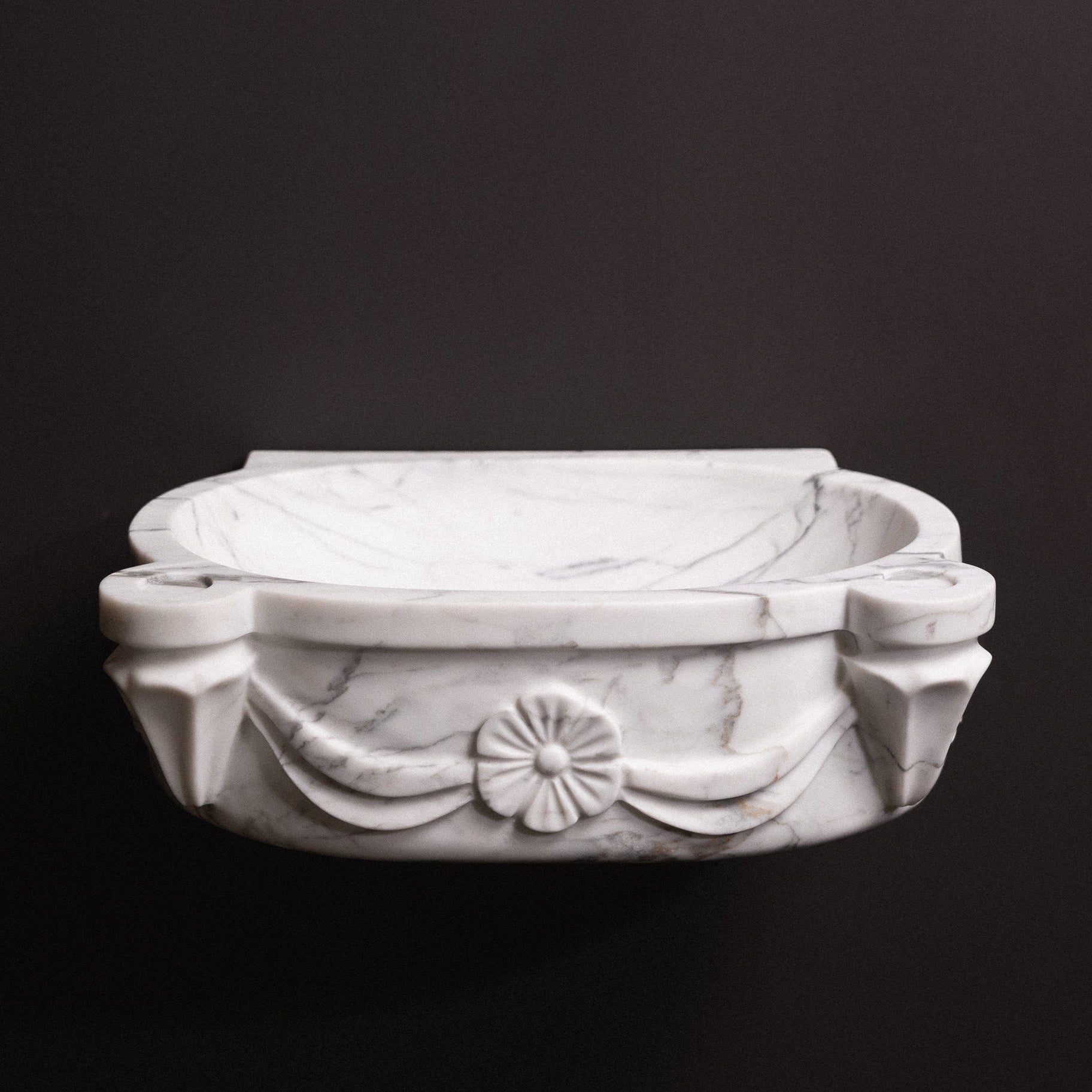 White statuary marble floating wall-mounted sink with floral rosette carvings and draped detailing — luxury hand-carved marble basin for bathrooms.